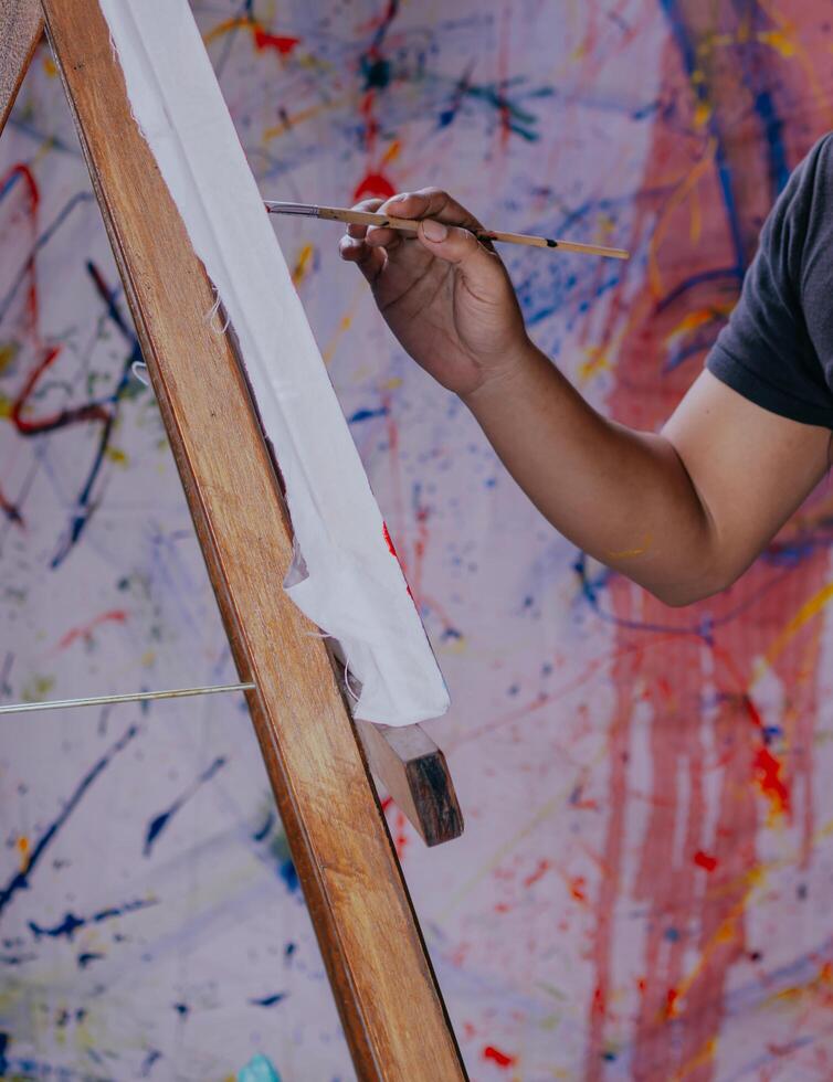 Close up of asian male painter at work painting on canvas in art studio. Creation and inspiration at an artists painting studio. photo
