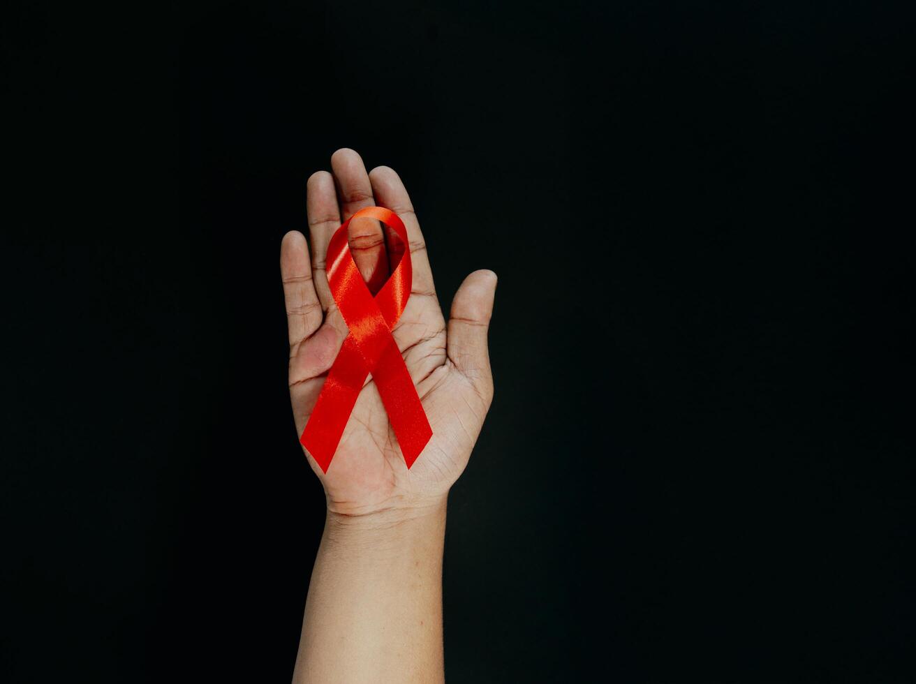 Woman with red awareness ribbon on black background, top view. Space for text. photo