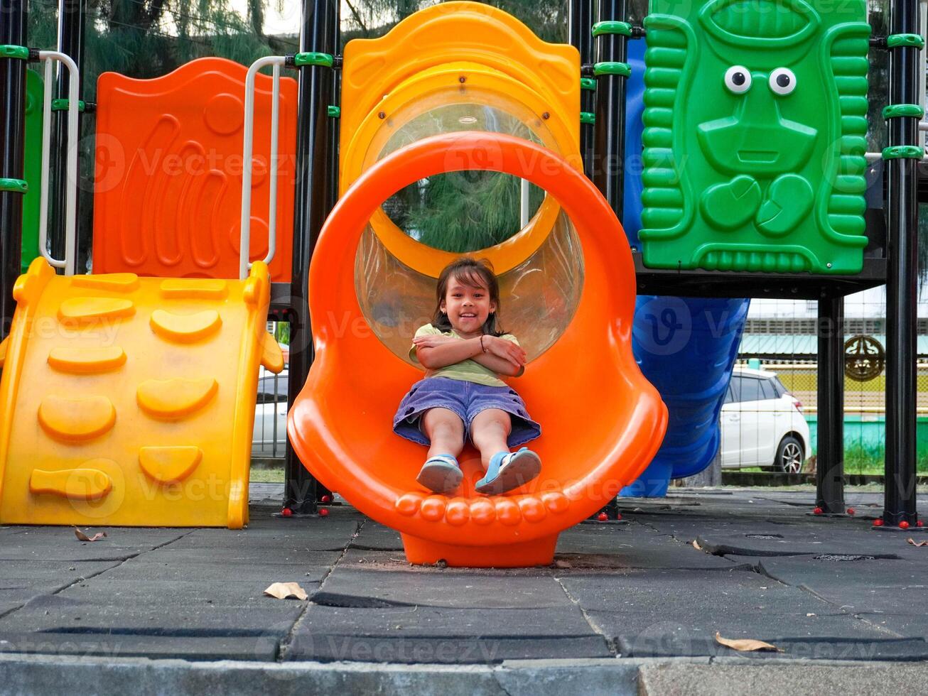 Children playing in the playground during summer vacation. Cute girl having fun on a colorful slide in an outdoor park. photo