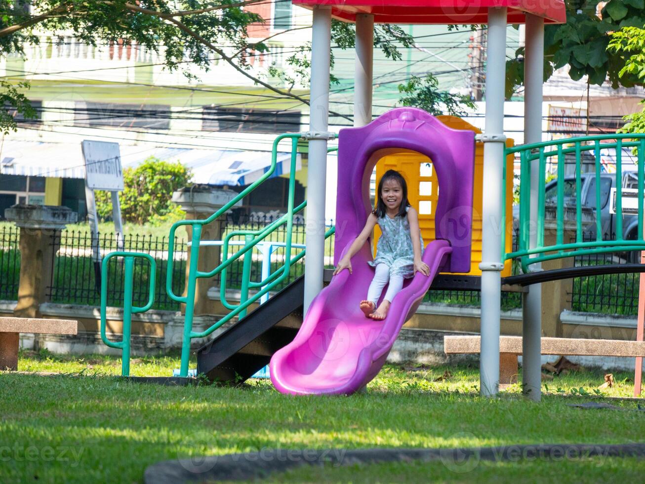 Cute girl having fun on a colorful slide in an outdoor park. Children playing in the playground during summer vacation. photo