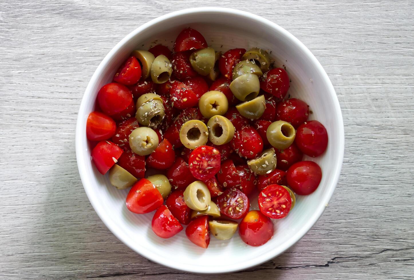 A vibrant salad of halved cherry tomatoes and halved green olives, seasoned with herbs. photo