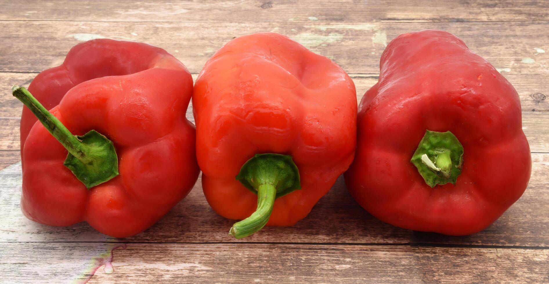 Close-up of three vibrant red bell peppers arranged on a rustic wooden surface. photo