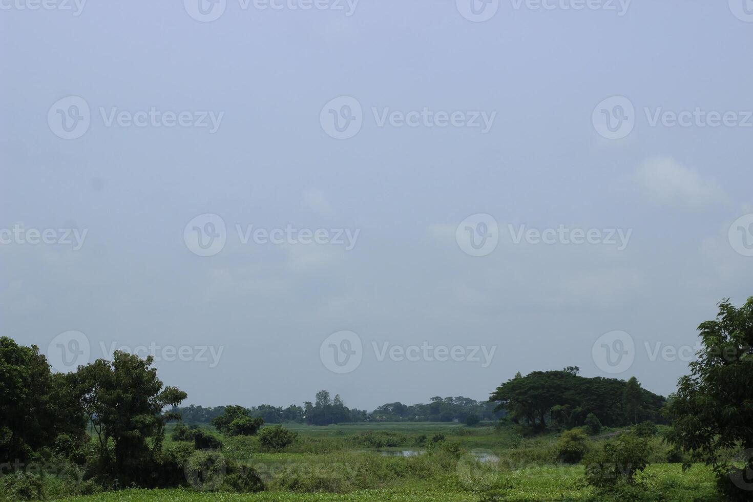 A wide, green landscape stretches under a hazy blue sky photo