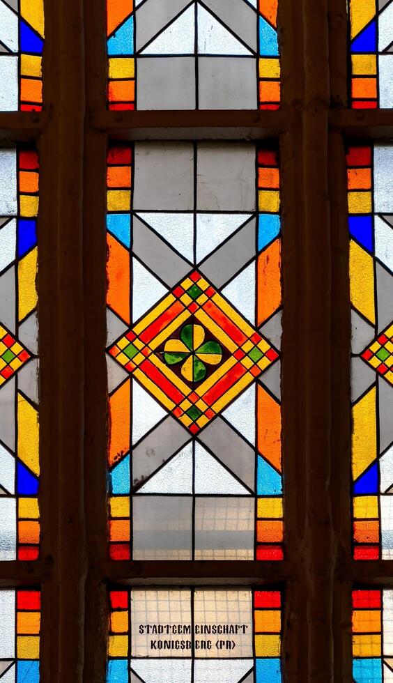 A close-up of an intricate stained glass window inside Konigsberg Cathedral in Kaliningrad. The geometric pattern features vibrant colors, including red, yellow, and blue, with a green clover design photo