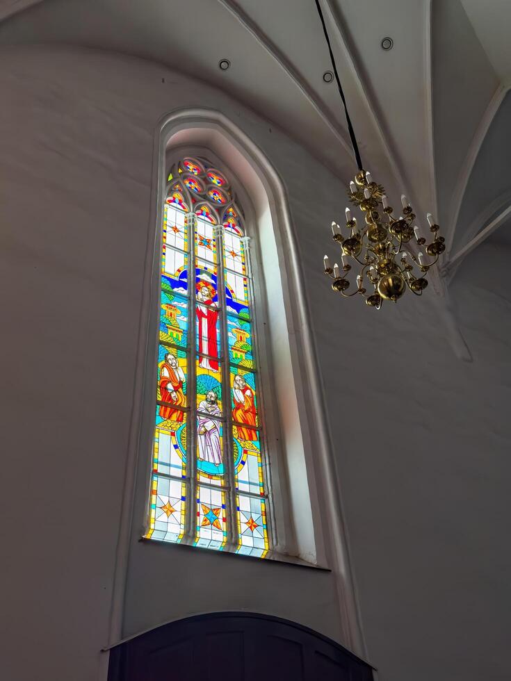 A pair of towering stained glass windows inside Konigsberg Cathedral in Kaliningrad, showcasing vibrant religious scenes and intricate geometric designs. The colorful panels depict various figures and photo