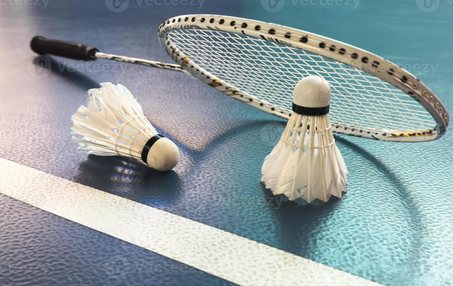 Cream white badminton shuttlecock and racket with neon light shading on floor in indoor badminton court, copy space, soft and selective focus. photo