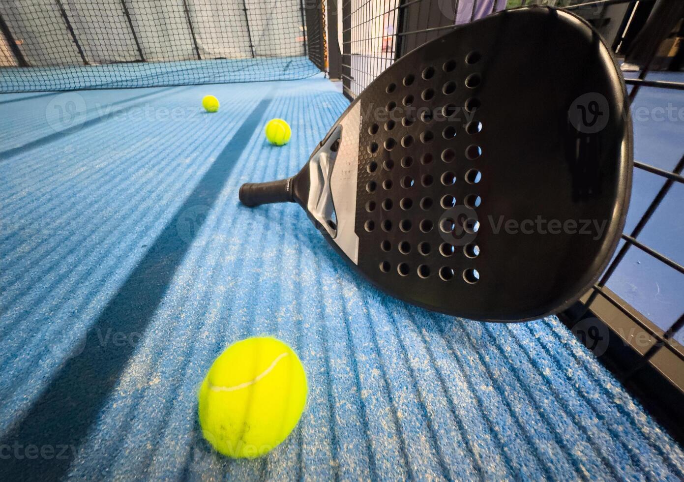 Padel racket and yellow ball behind net on a green court grass turf outdoors at sunset. Paddle is a racquet game. Professional sport concept with space for text photo
