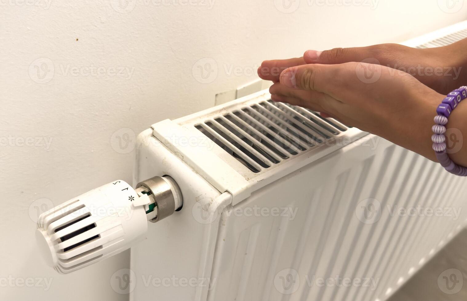 Closeup of woman warming her hands on the heater at home during cold winter days, top view. Female getting warm up her arms over radiator. Concept of heating season, cold weather. photo
