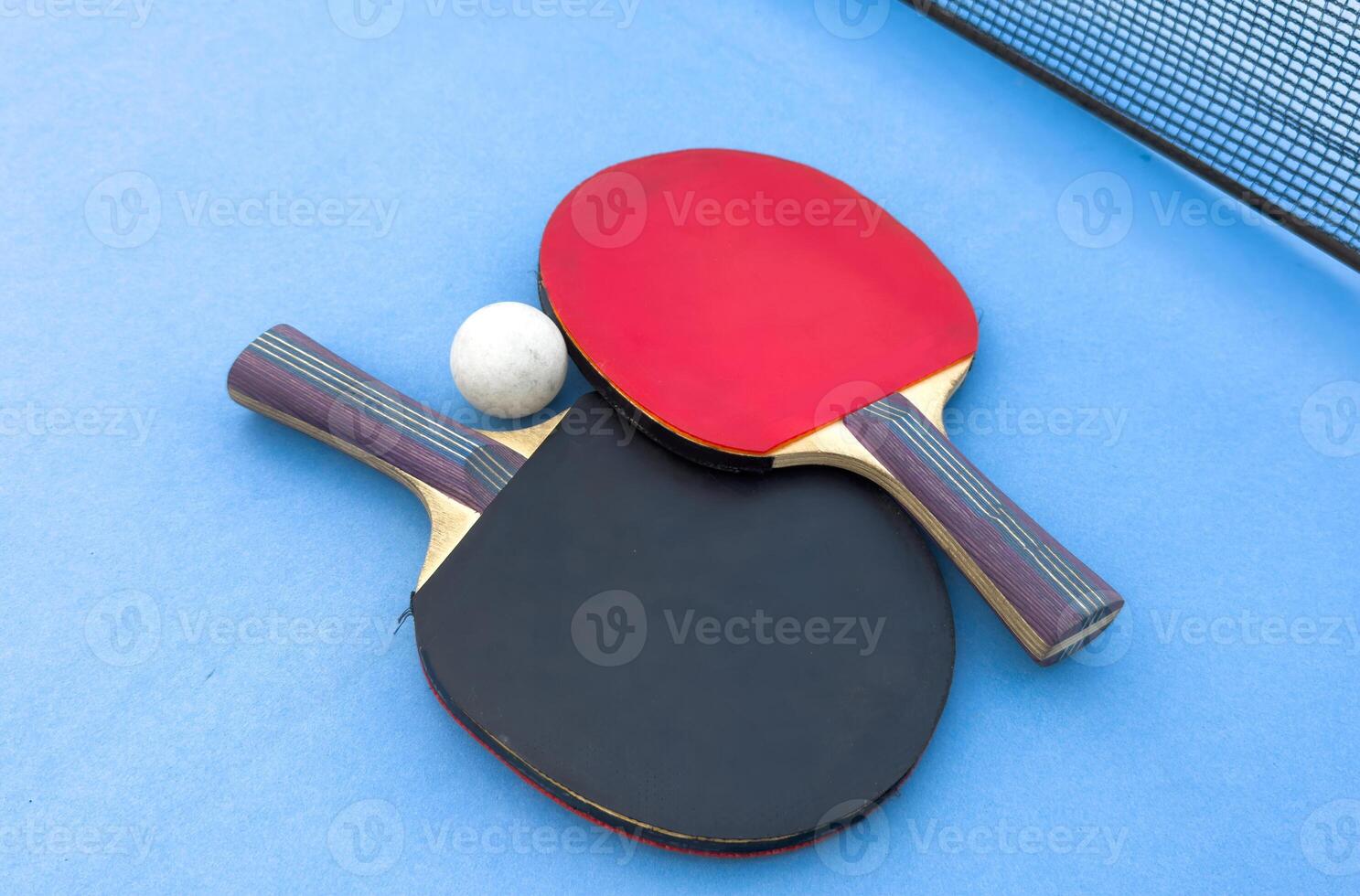 Red and black rackets for table tennis with white ball on blue background. Ping pong sports equipment in minimal style. Flat lay, top view, copy space photo