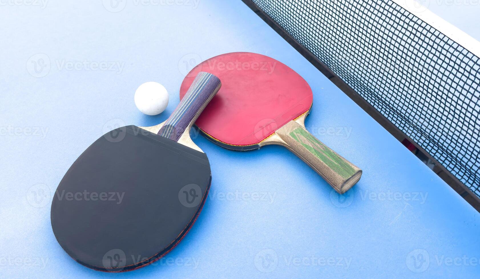 Red and black rackets for table tennis with white ball on blue background. Ping pong sports equipment in minimal style. Flat lay, top view, copy space photo