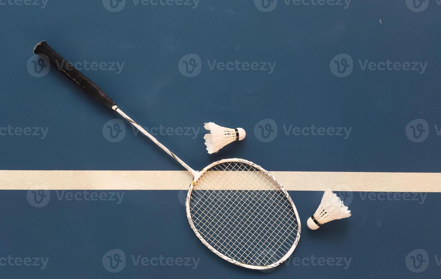 Cream white badminton shuttlecock and racket with neon light shading on dark floor in indoor badminton court, copy space, soft and selective focus. photo