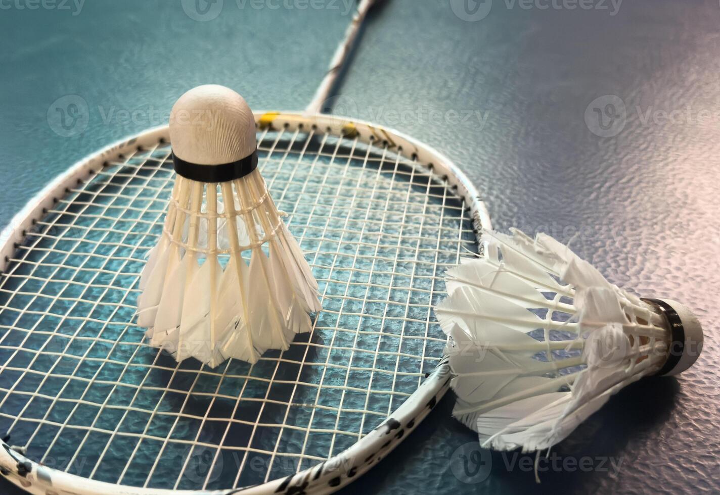 Cream white badminton shuttlecock and racket with neon light shading on dark floor in indoor badminton court, copy space, soft and selective focus. photo