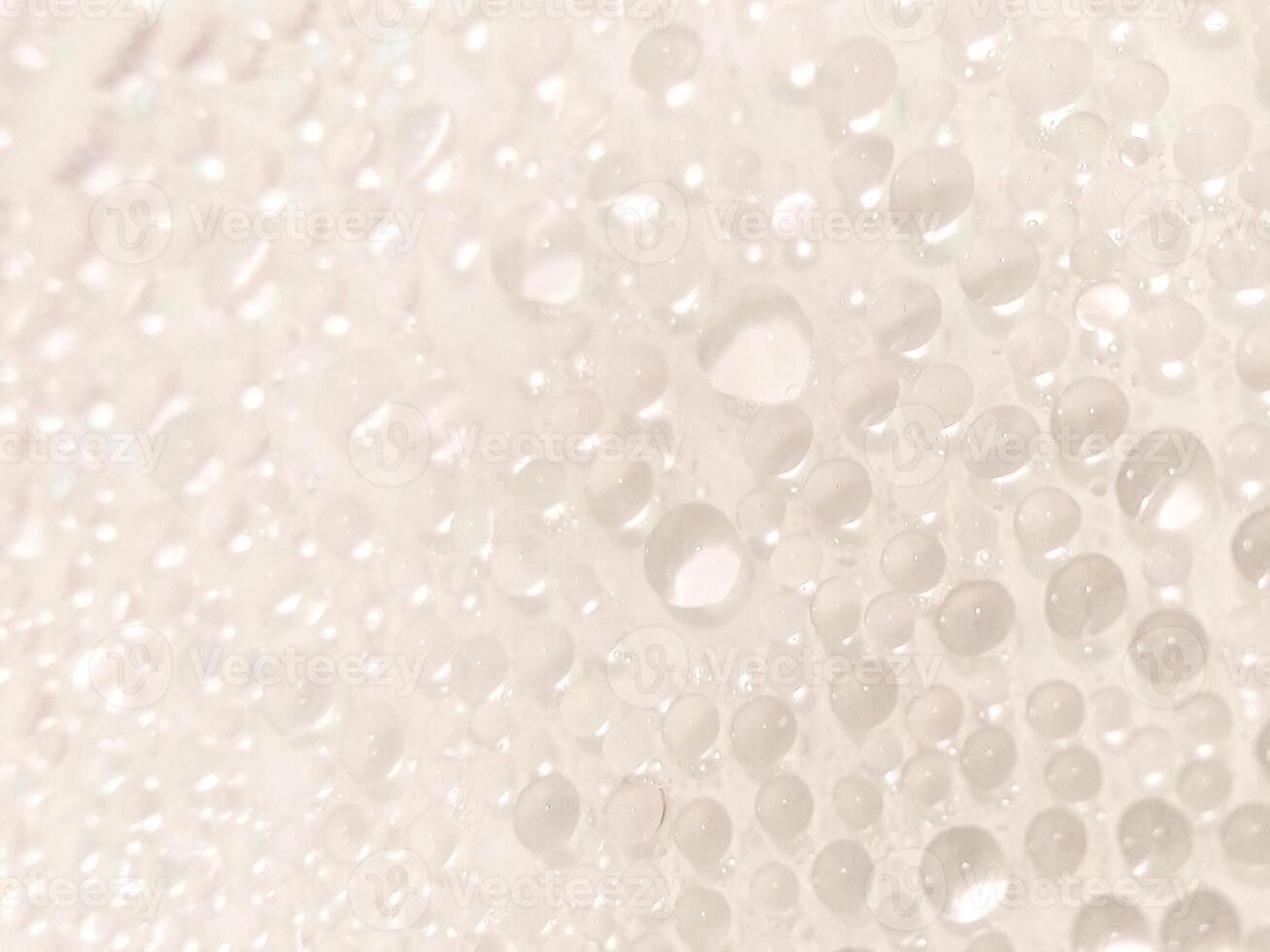 A close-up view of numerous water droplets on a transparent surface, creating a soft, dreamy texture with a white and pastel background. photo