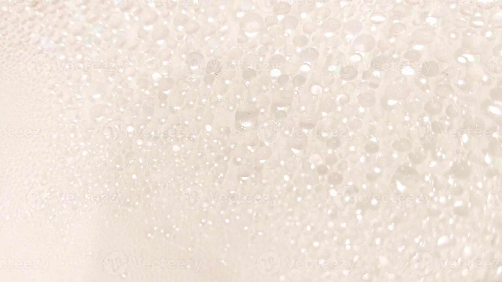 A close-up view of numerous water droplets on a transparent surface, creating a soft, dreamy texture with a white and pastel background. photo