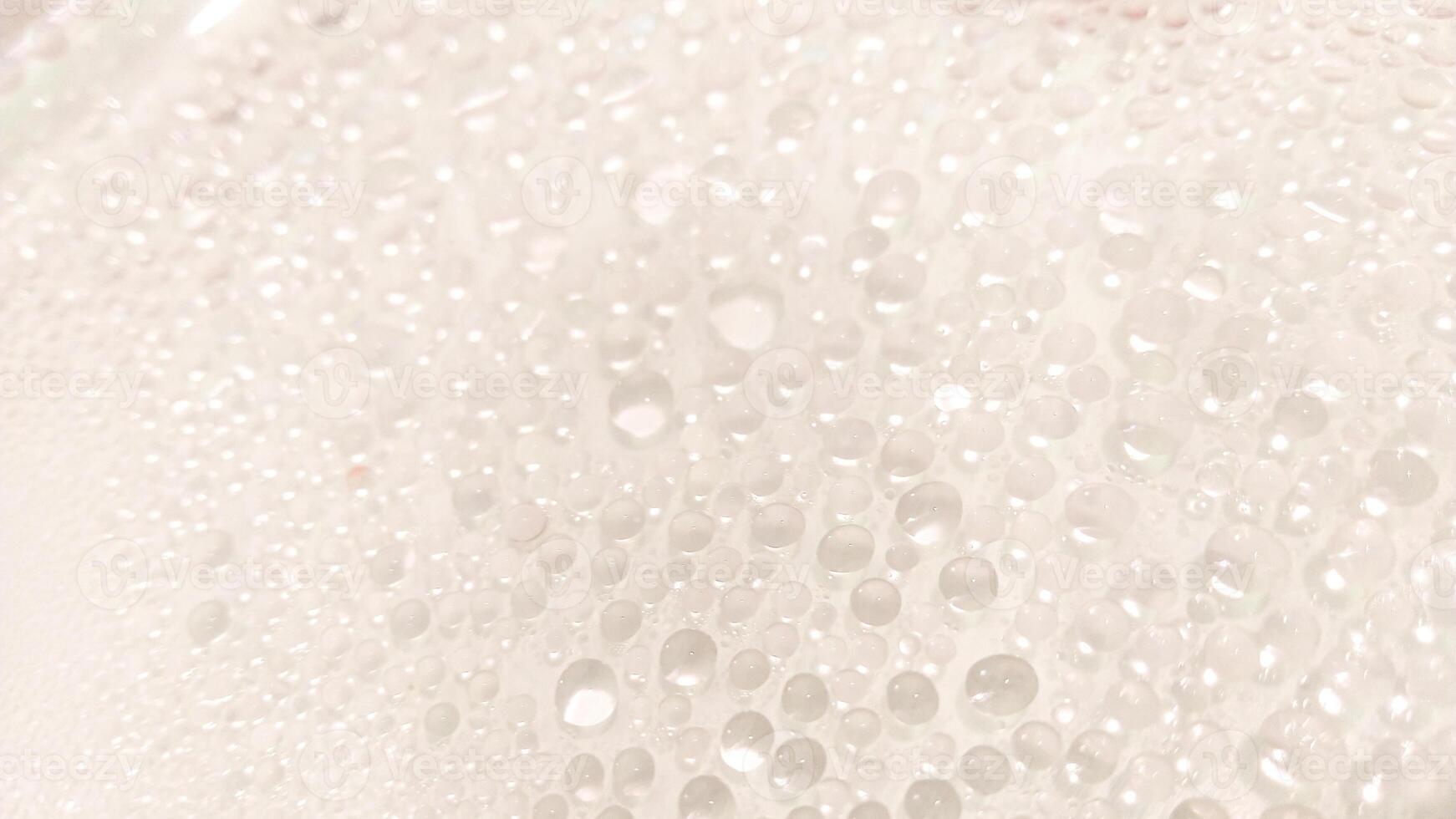 A close-up view of numerous water droplets on a transparent surface, creating a soft, dreamy texture with a white and pastel background. photo