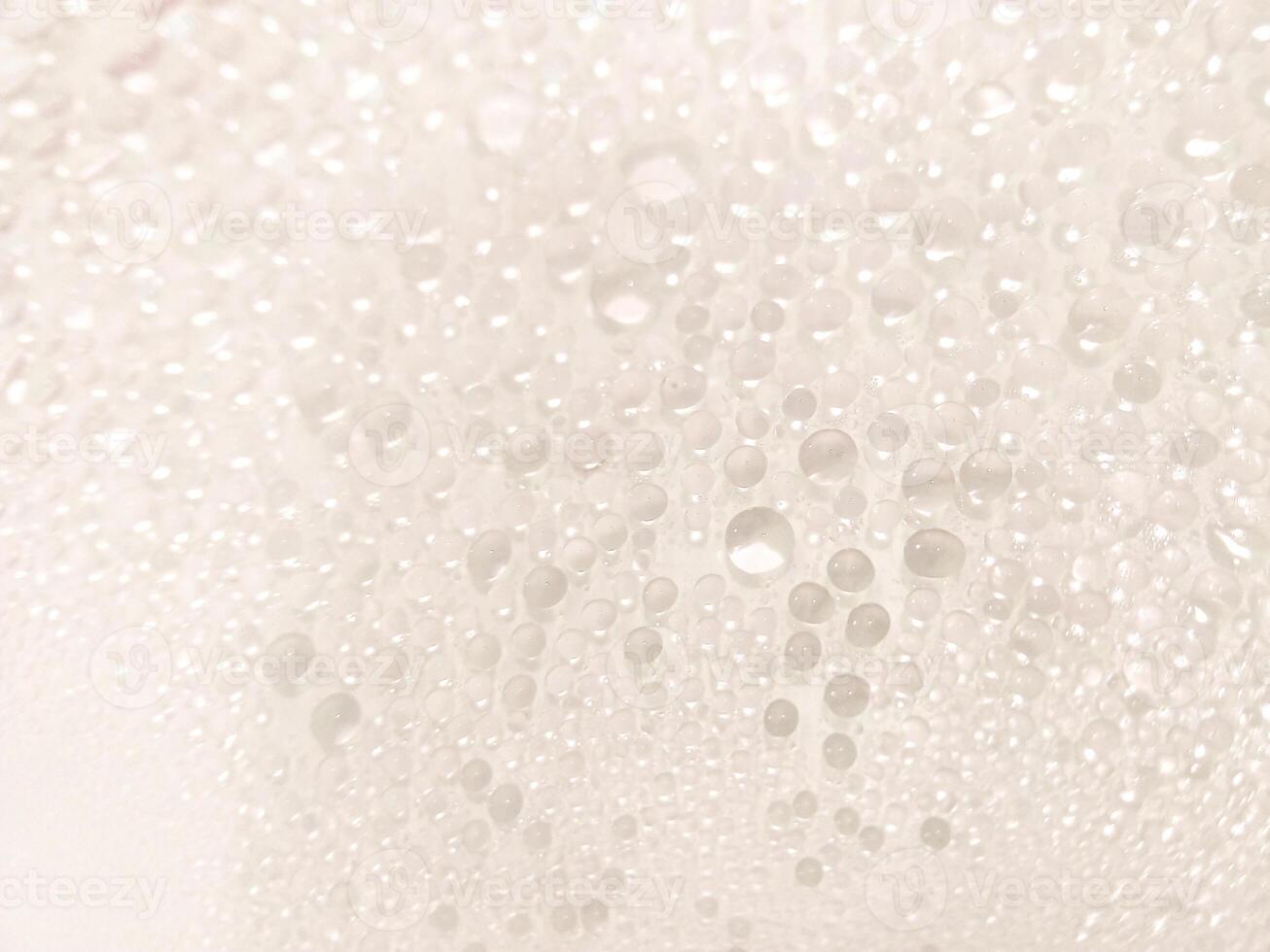 A close-up view of numerous water droplets on a transparent surface, creating a soft, dreamy texture with a white and pastel background. photo