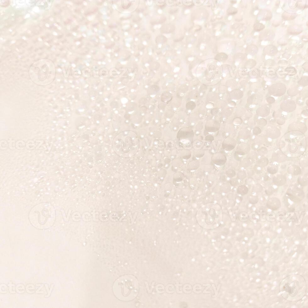 A close-up view of numerous water droplets on a transparent surface, creating a soft, dreamy texture with a white and pastel background. photo