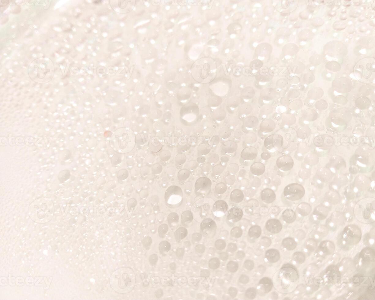 A close-up view of numerous water droplets on a transparent surface, creating a soft, dreamy texture with a white and pastel background. photo