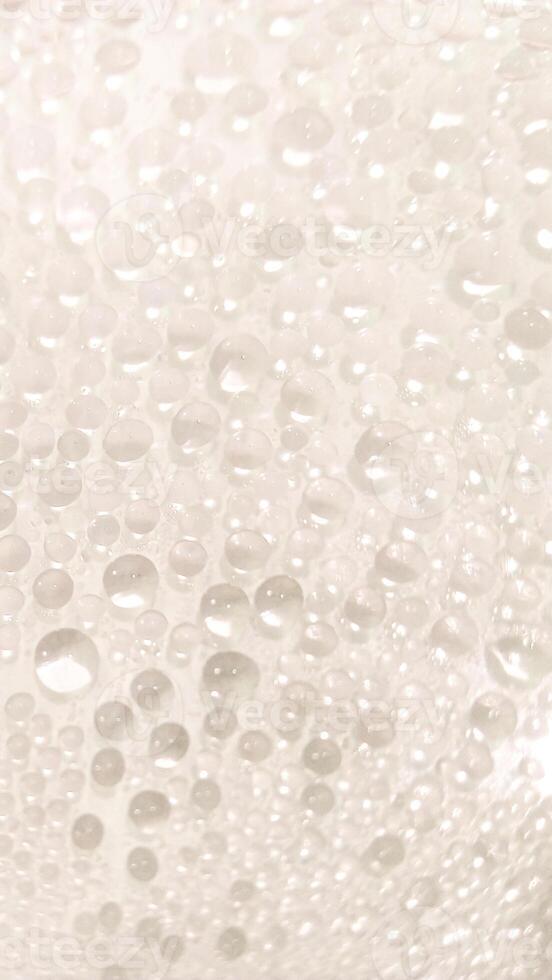 A close-up view of numerous water droplets on a transparent surface, creating a soft, dreamy texture with a white and pastel background. photo
