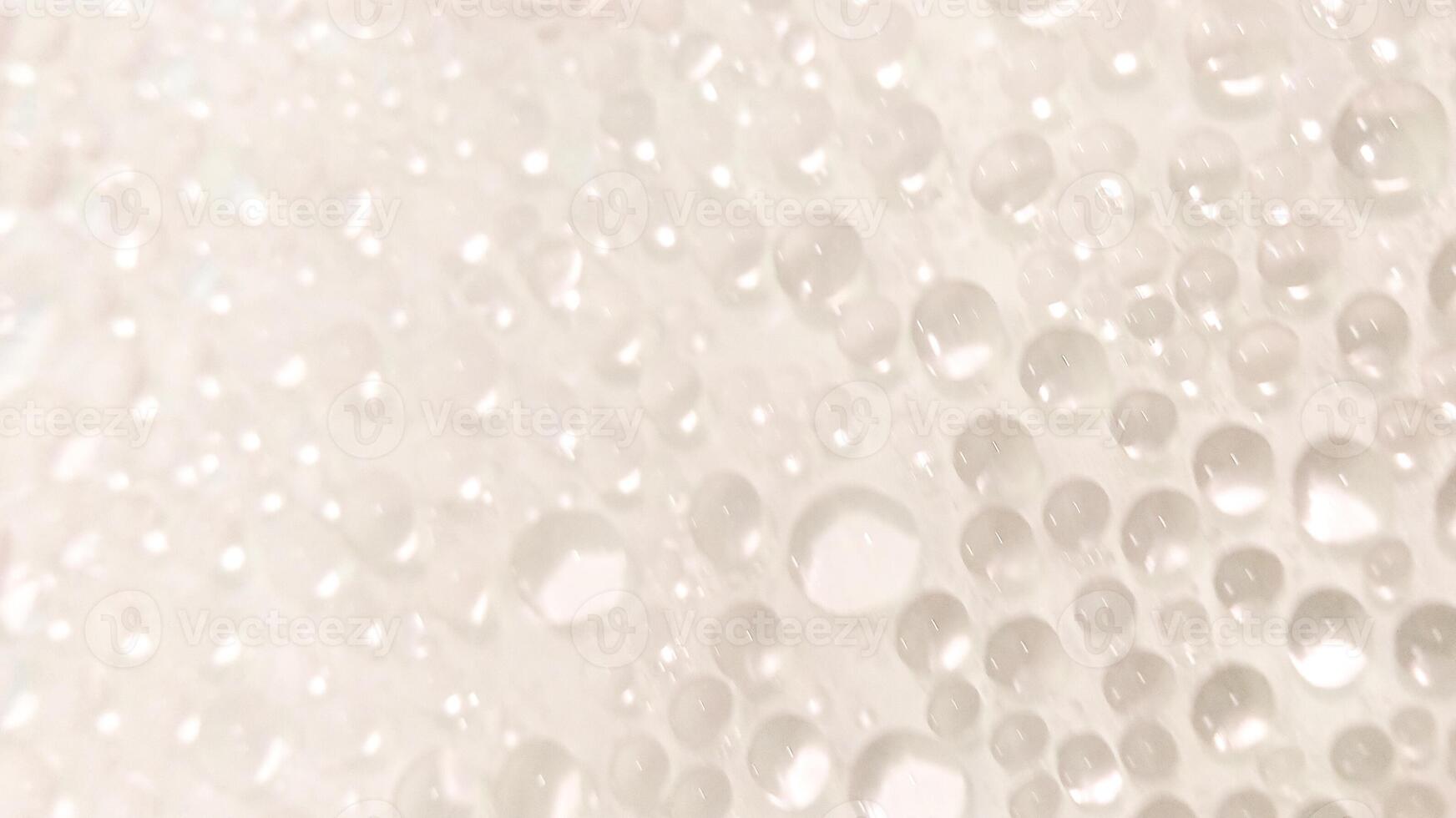 A close-up view of numerous water droplets on a transparent surface, creating a soft, dreamy texture with a white and pastel background. photo