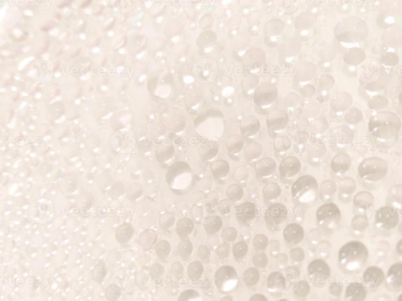 A close-up view of numerous water droplets on a transparent surface, creating a soft, dreamy texture with a white and pastel background. photo