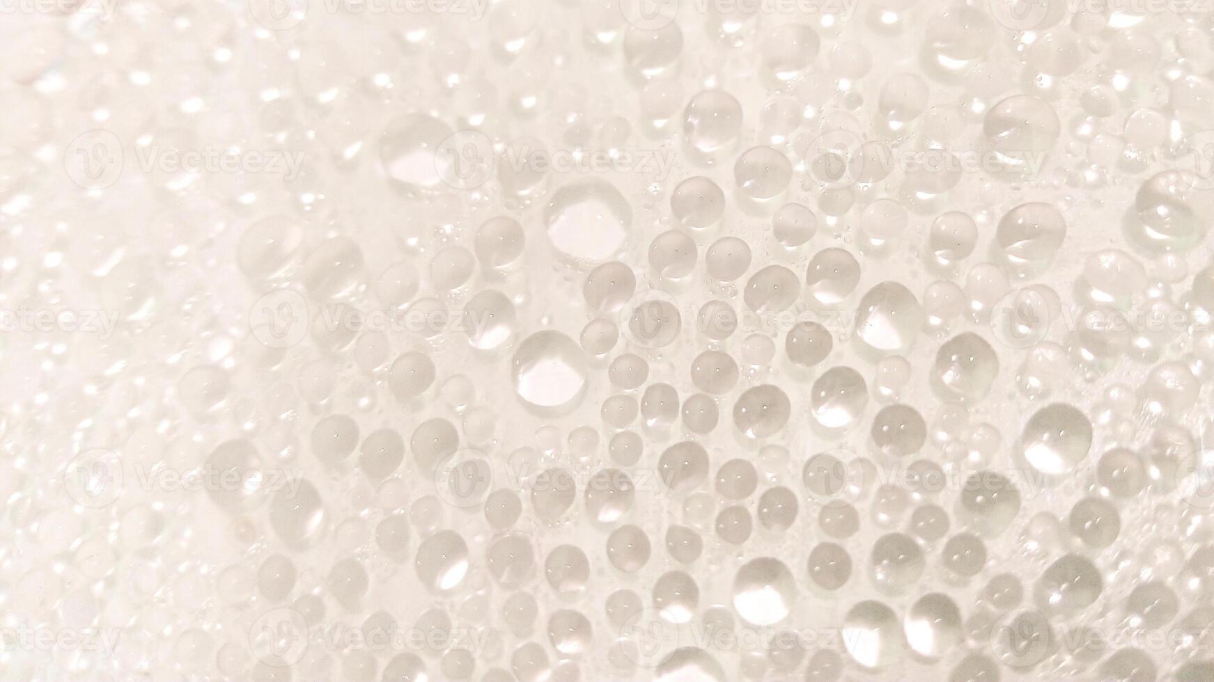 A close-up view of numerous water droplets on a transparent surface, creating a soft, dreamy texture with a white and pastel background. photo