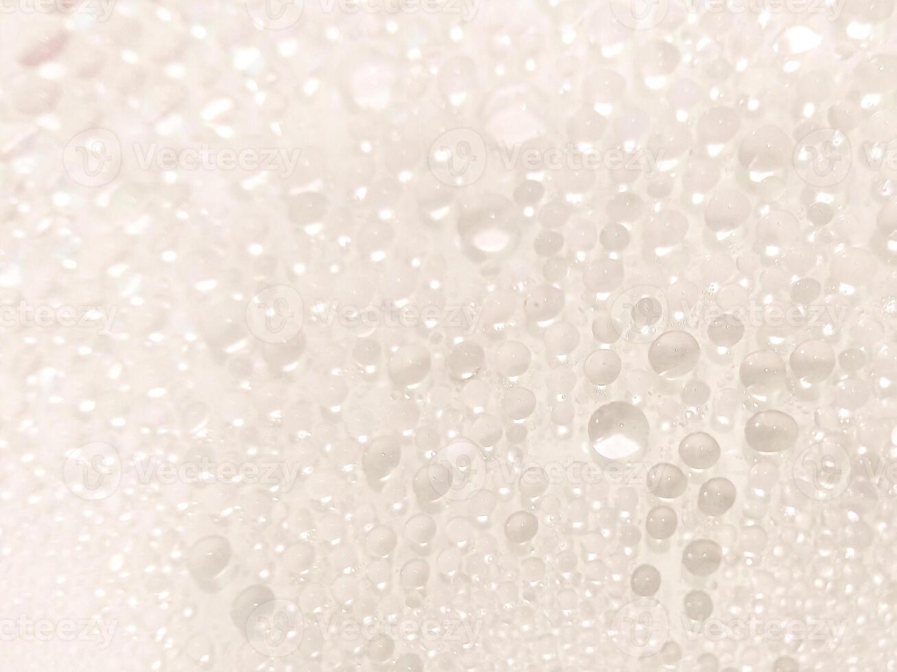 A close-up view of numerous water droplets on a transparent surface, creating a soft, dreamy texture with a white and pastel background. photo