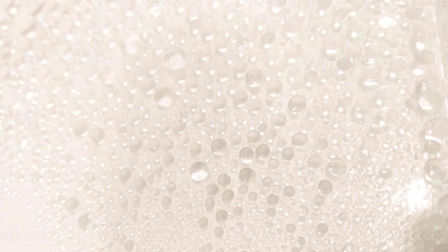 A close-up view of numerous water droplets on a transparent surface, creating a soft, dreamy texture with a white and pastel background. photo