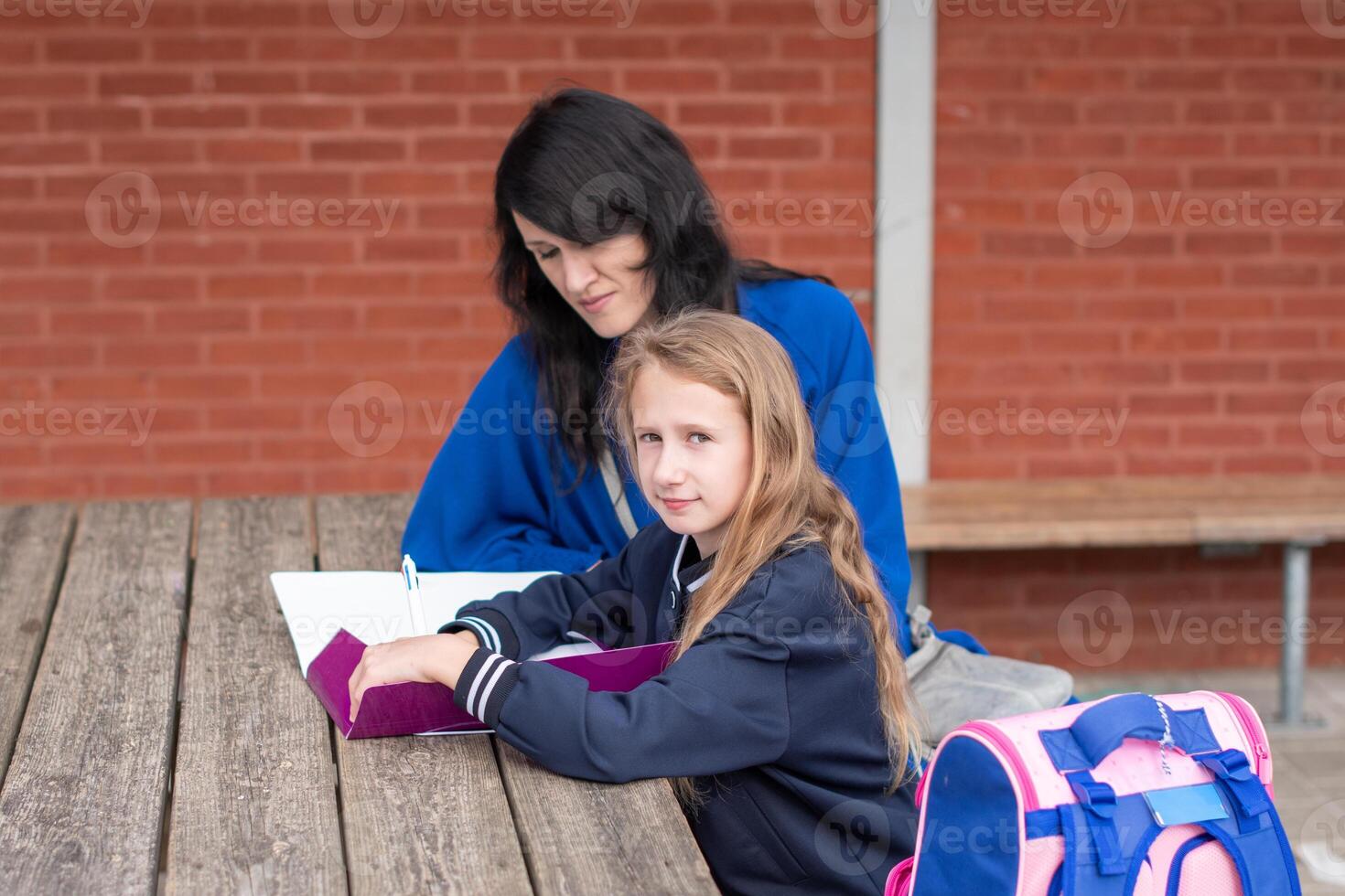 mother helping daughter with homework at wooden table in children playground doing homework, education concept, back to school, photo