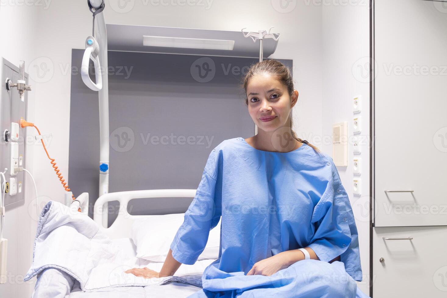 young woman in a private hospital room, dressed in a blue gown, sits on a bed and waits to be examined by a doctor before plastic surgery, photo