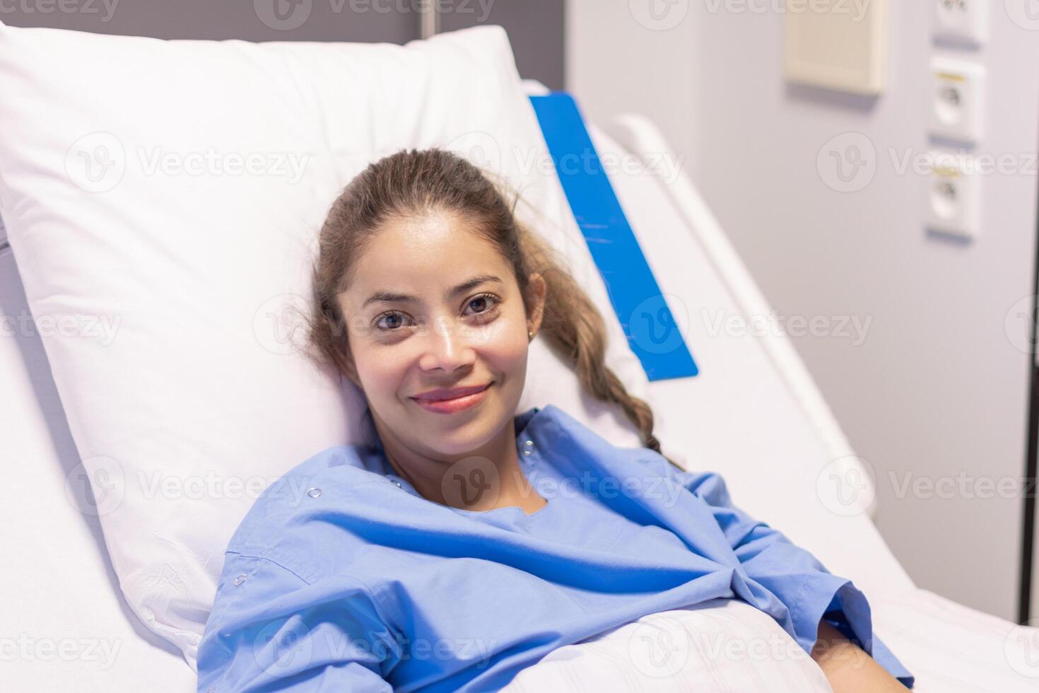 young beautiful woman in private hospital room, dressed in blue robe, sits on bed and rejoices at quick correction of cosmetic defect, waits for doctor's examination before plastic surgery, photo