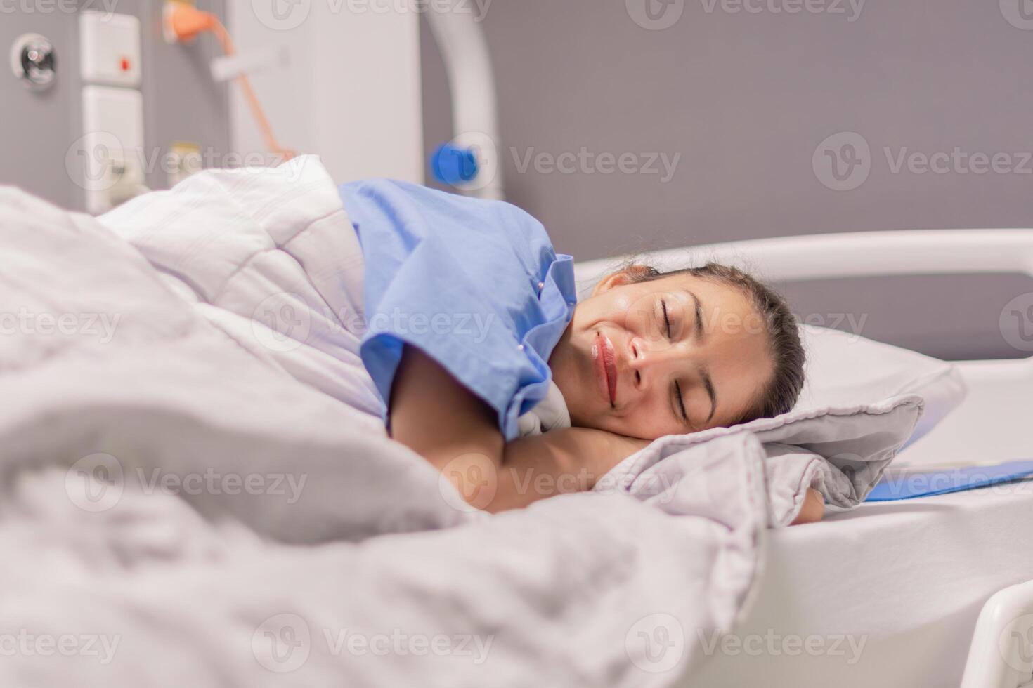 Young woman in blue robe lying comfortably and getting ready for bed on hospital bed in calm environment of clinic in private room, soft lighting, concept of recovery and care, photo