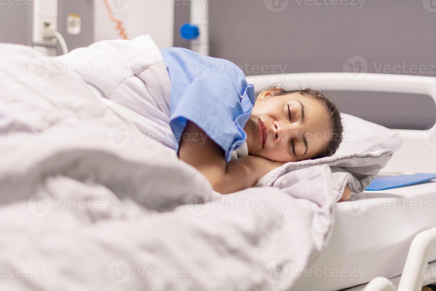 Young woman in blue robe lying comfortably and getting ready for bed on hospital bed in calm environment of clinic in private room, soft lighting, concept of recovery and care, photo