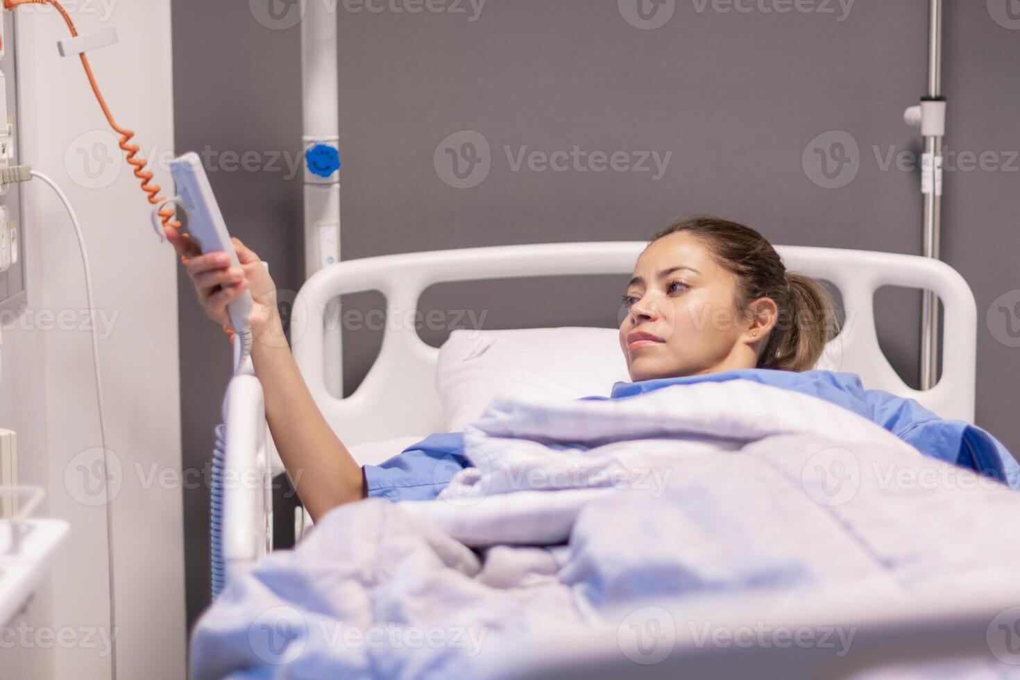 Young female patient in blue gown pressing emergency call button for medical staff, nurse to help with changing position in bed, soft lighting, recovery and care concept, photo