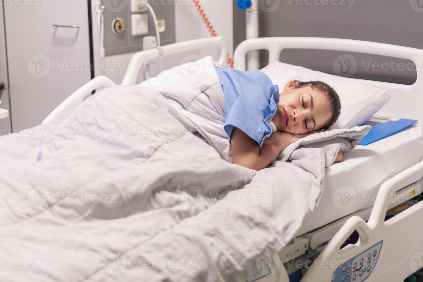 Young woman in blue robe lying comfortably and getting ready for bed on hospital bed in calm environment of clinic in private room, soft lighting, concept of recovery and care, photo