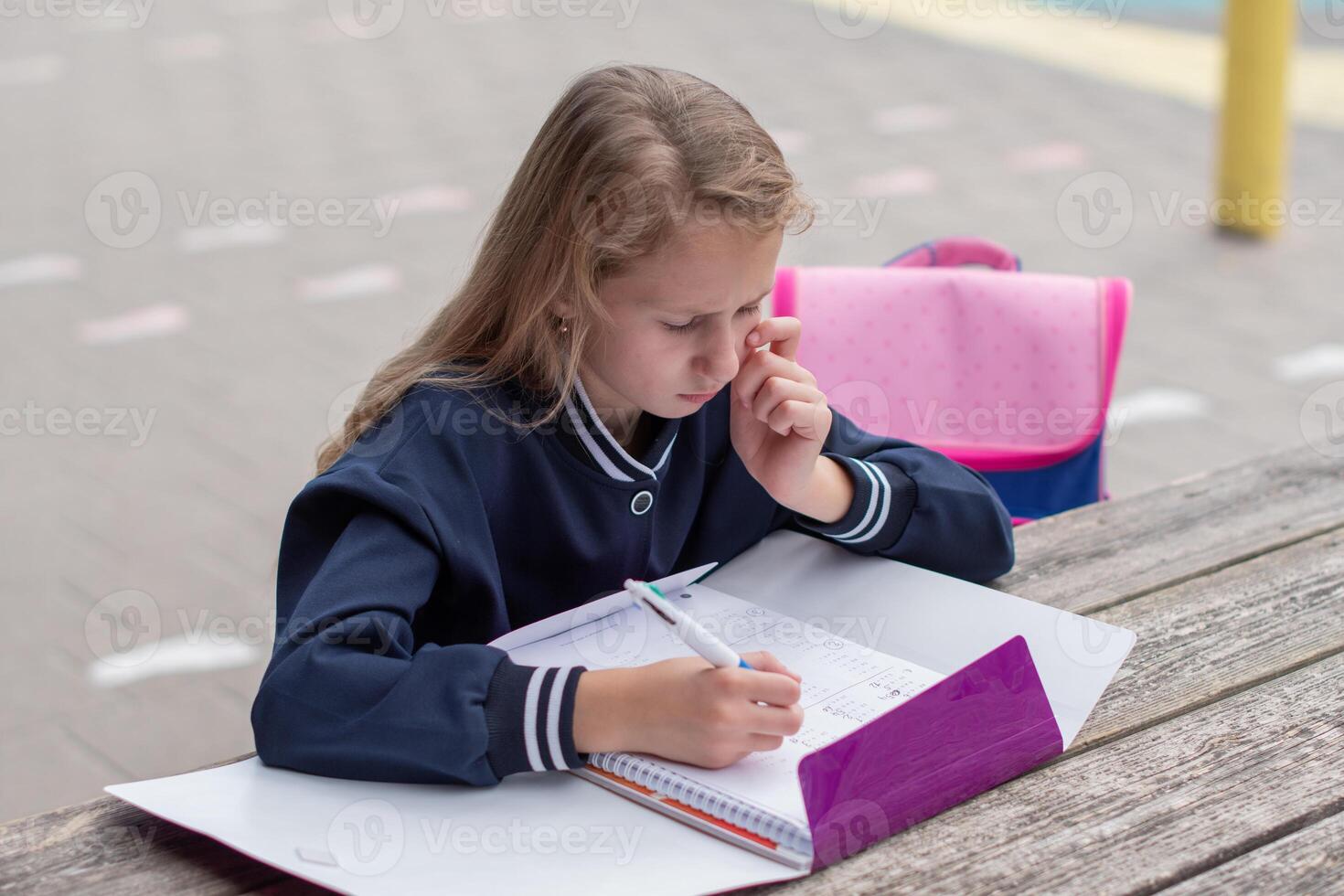 Teenage girl focused on solving complex math equation at wooden table in park outdoors, education concept, back to school, girl in beautiful blue uniform and with purple notebook photo