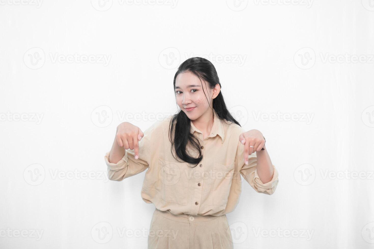 Expression of Indonesian Asian model woman in white dress smiling and pointing down photo