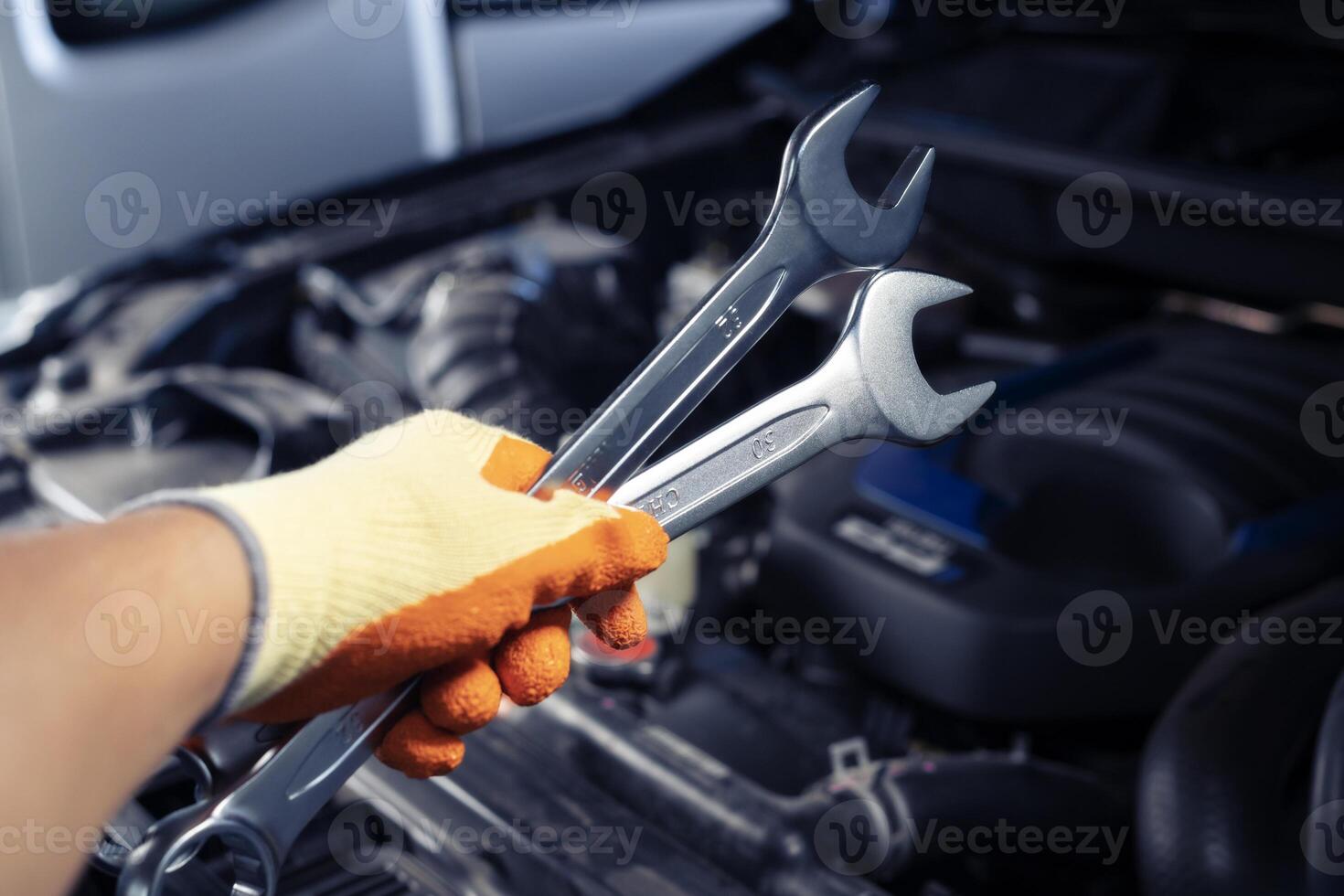 Auto mechanic holding a wrench is repairing a car. Car care and service, professional car mechanic holds wrench to fix parts and repair car engine. photo