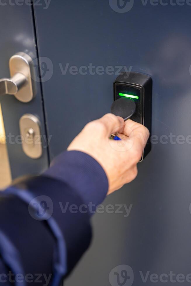 Close up view of person using a electric lock key fob to access a building via a reader of entry system mounted on a house wall. High quality photo
