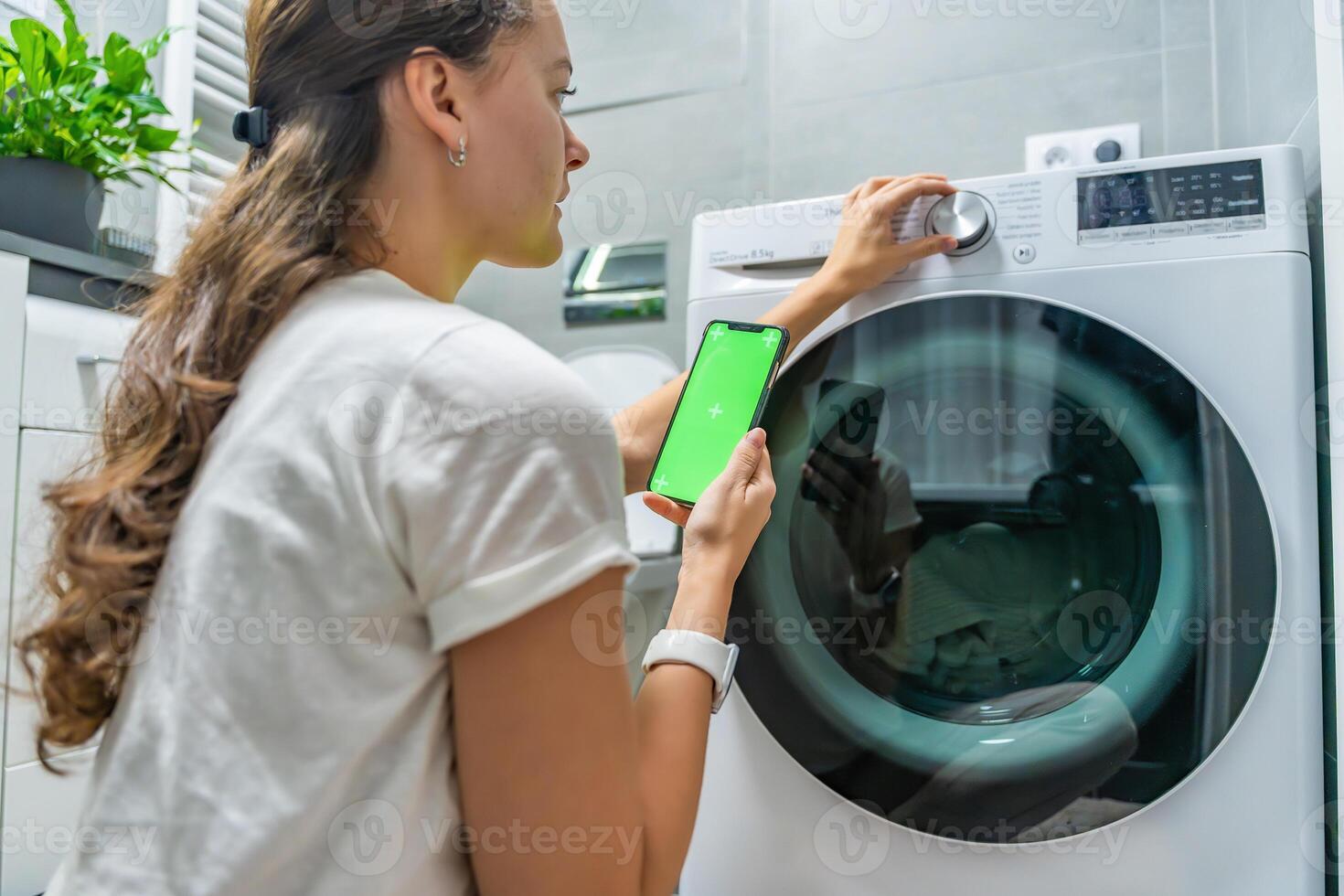 Young woman using mobile phone control via wi-fi and app for washing machine in home. Homesmart app, chroma key green screen photo
