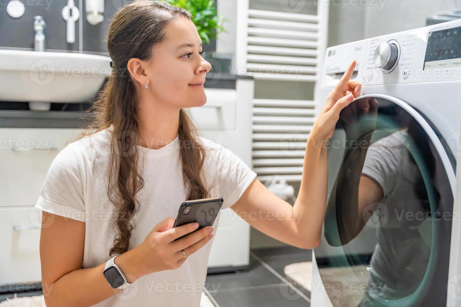 Young woman using mobile phone control via wi-fi and app for washing machine in home. Homesmart and new technology concept photo