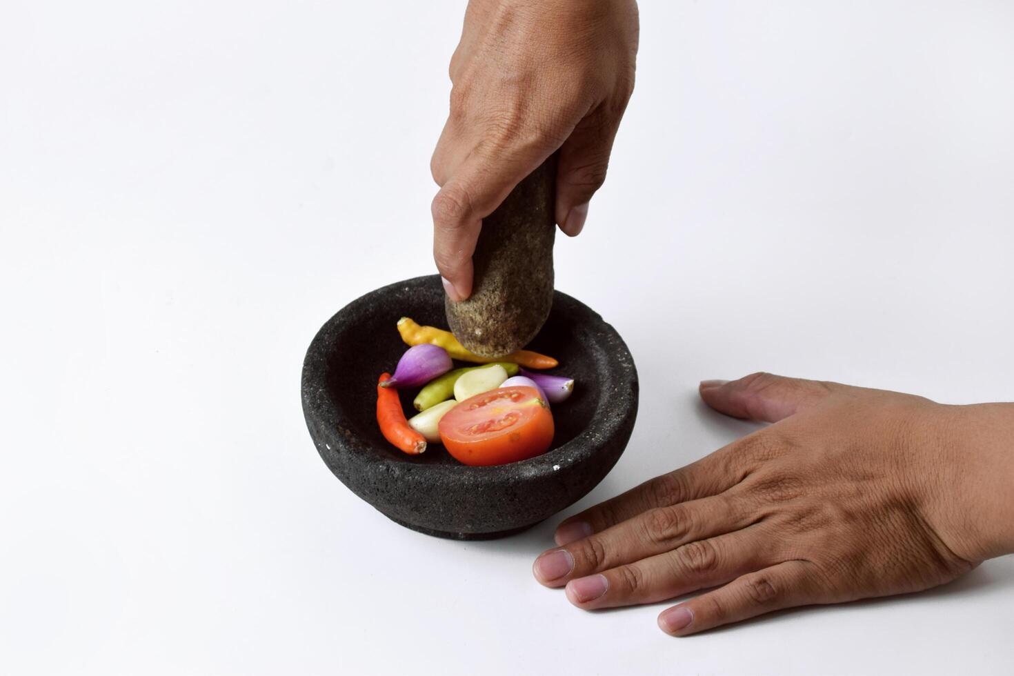 A man uses two hands to make chili sauce in a mortar made of stone photo