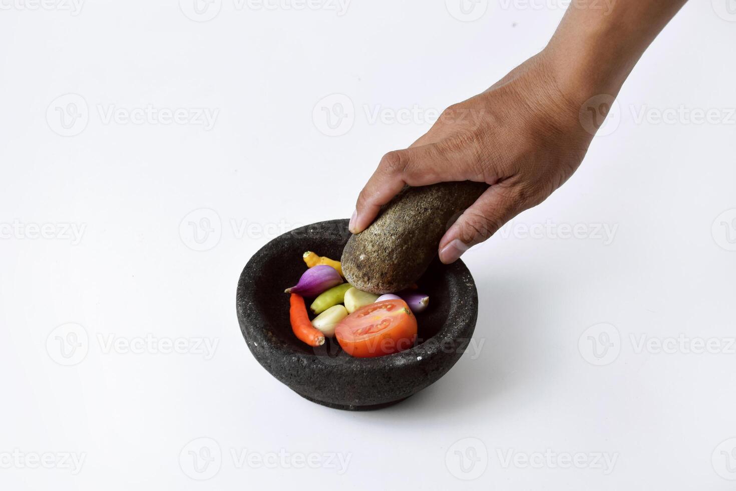 A man's hands are making chili sauce in a mortar made of stone photo