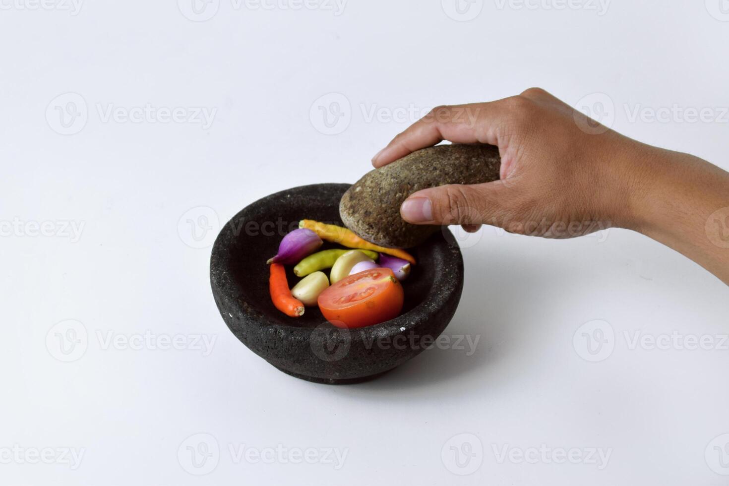 Someone's hands make chili sauce in a mortar made of stone on white background photo