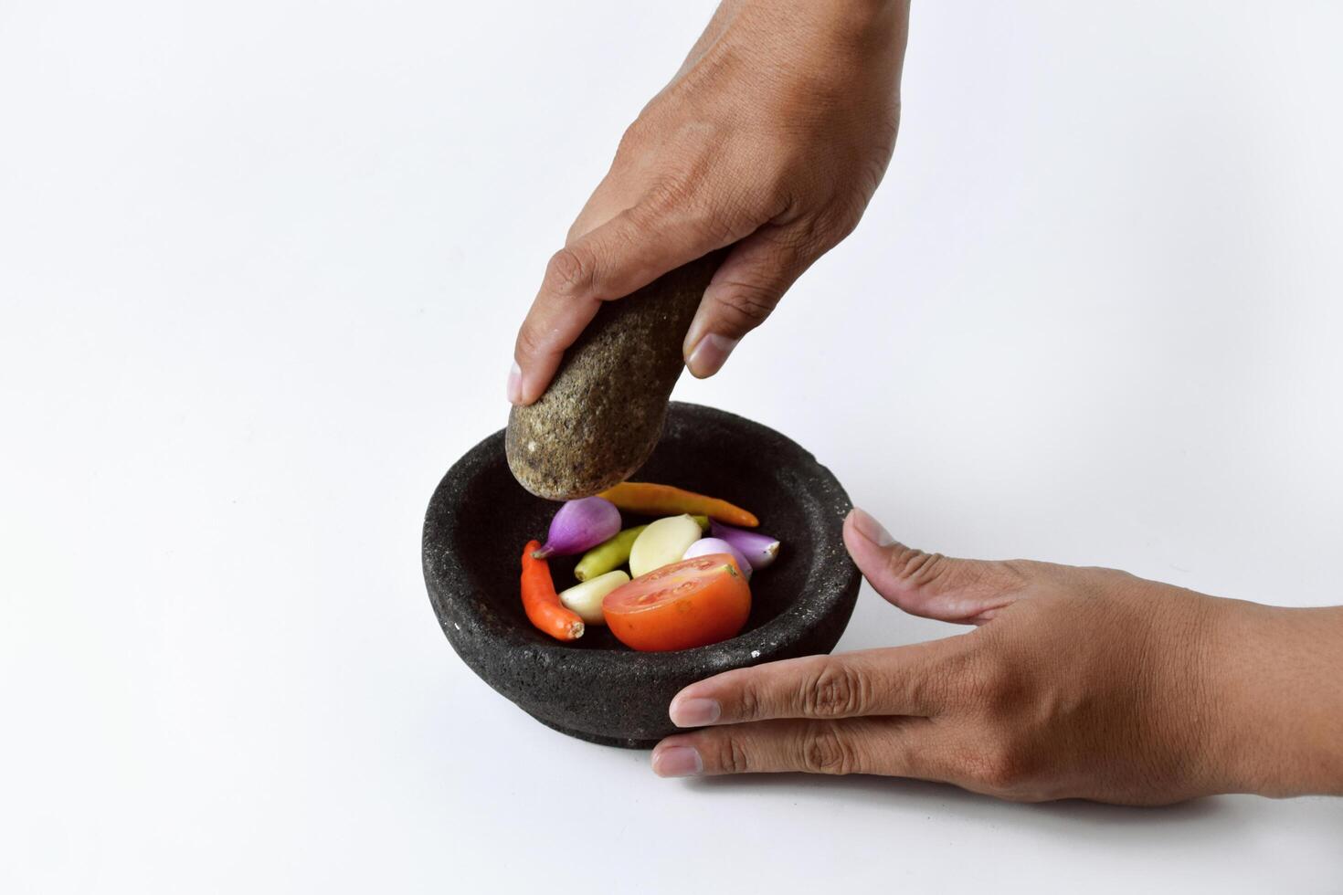 A man uses two hands to make chili sauce in a mortar made of stone photo