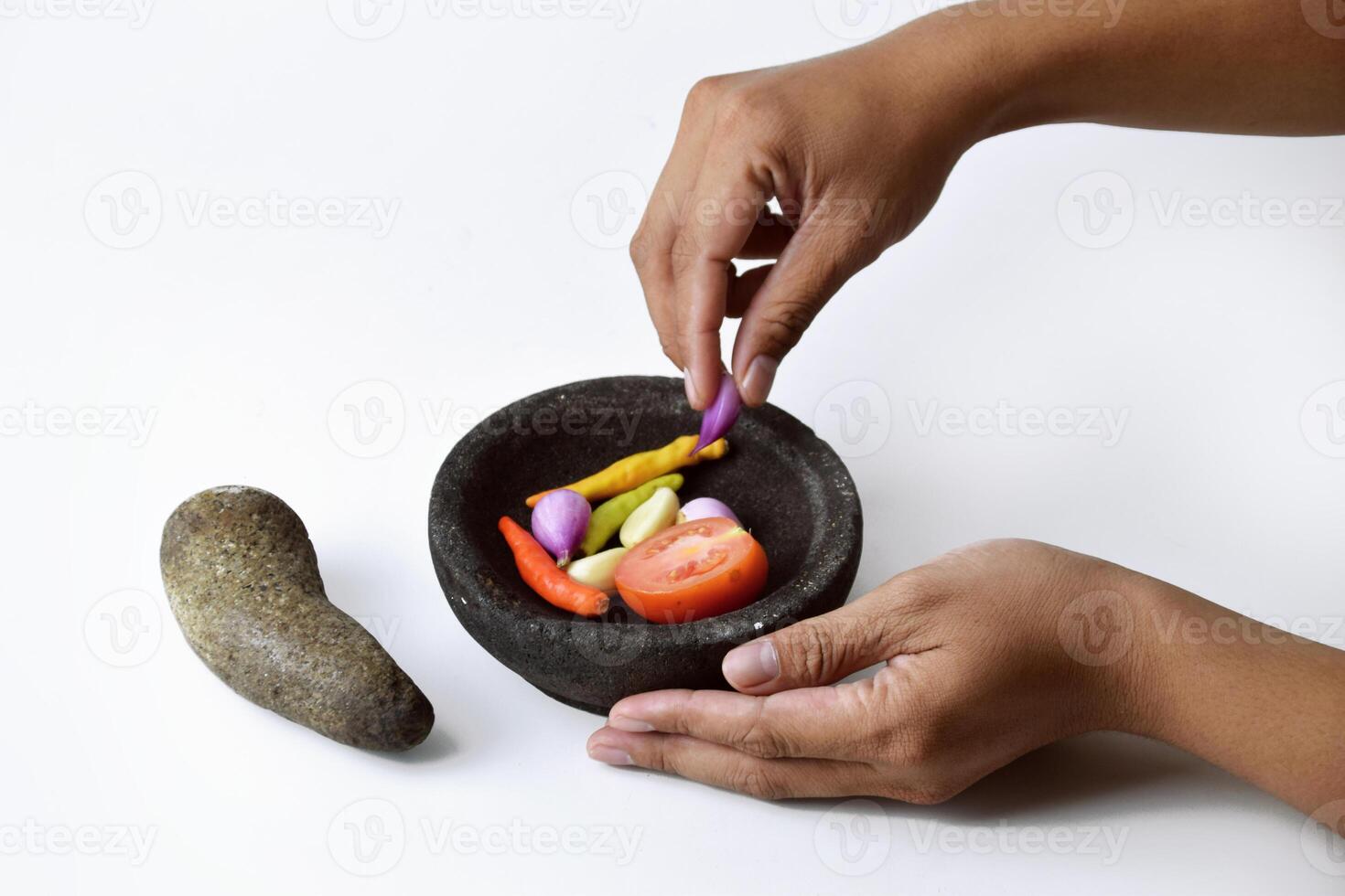 A man shows the ingredients for making chili in a mortar made of stone photo