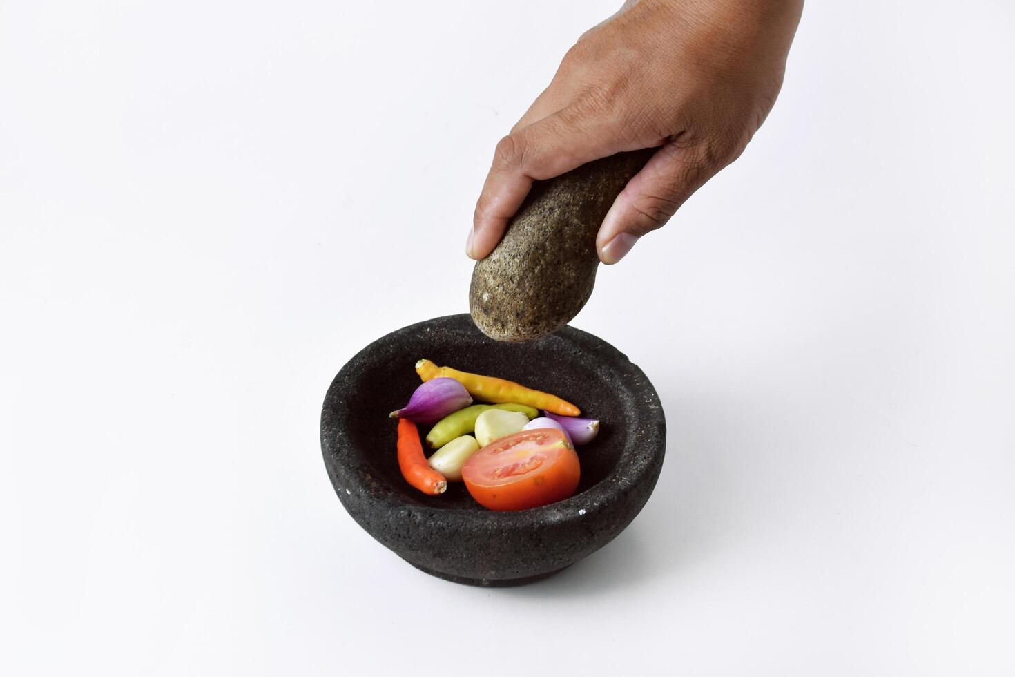A man's hands are making chili sauce in a mortar made of stone photo