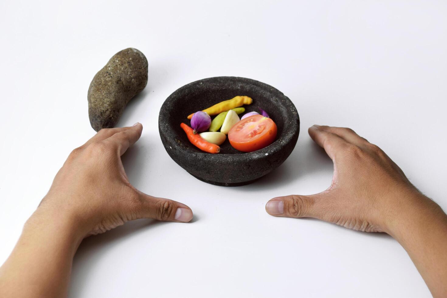 A man shows the ingredients for making chili sauce in a mortar made of stone photo