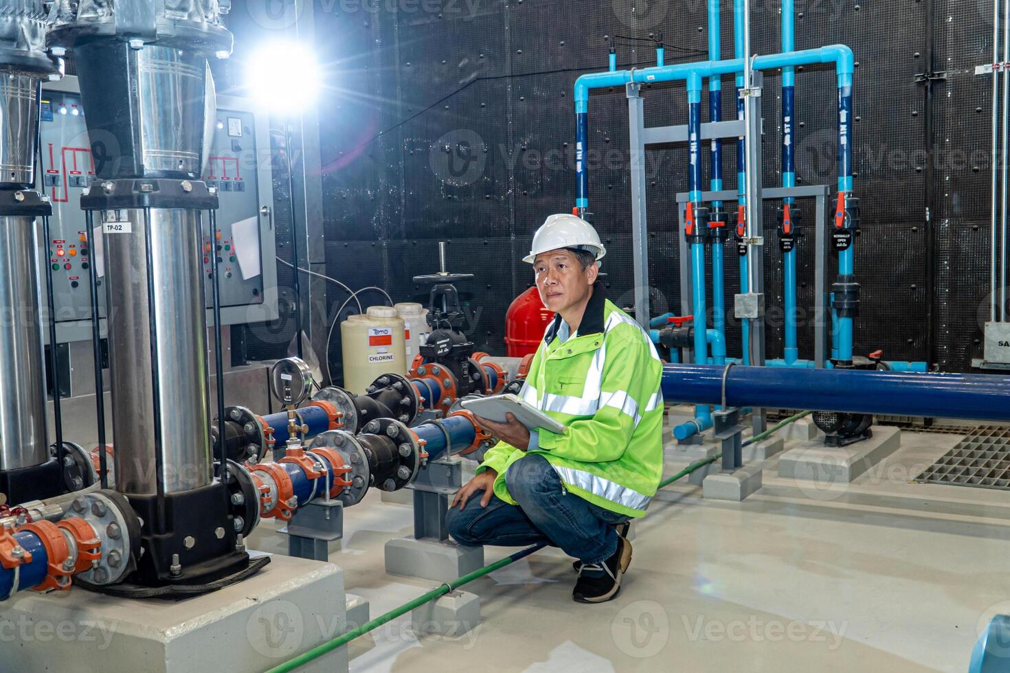 asian man worker in protective uniform and with hardhat using tablet for checking temperature in pipes Factory interior. photo