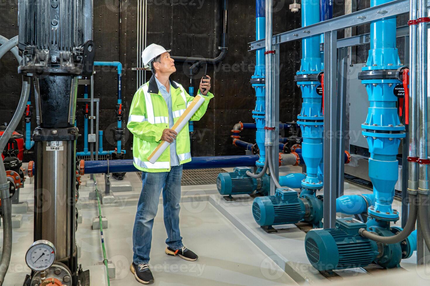 asian man worker in protective uniform and with hardhat using tablet for checking temperature in pipes Factory interior. photo